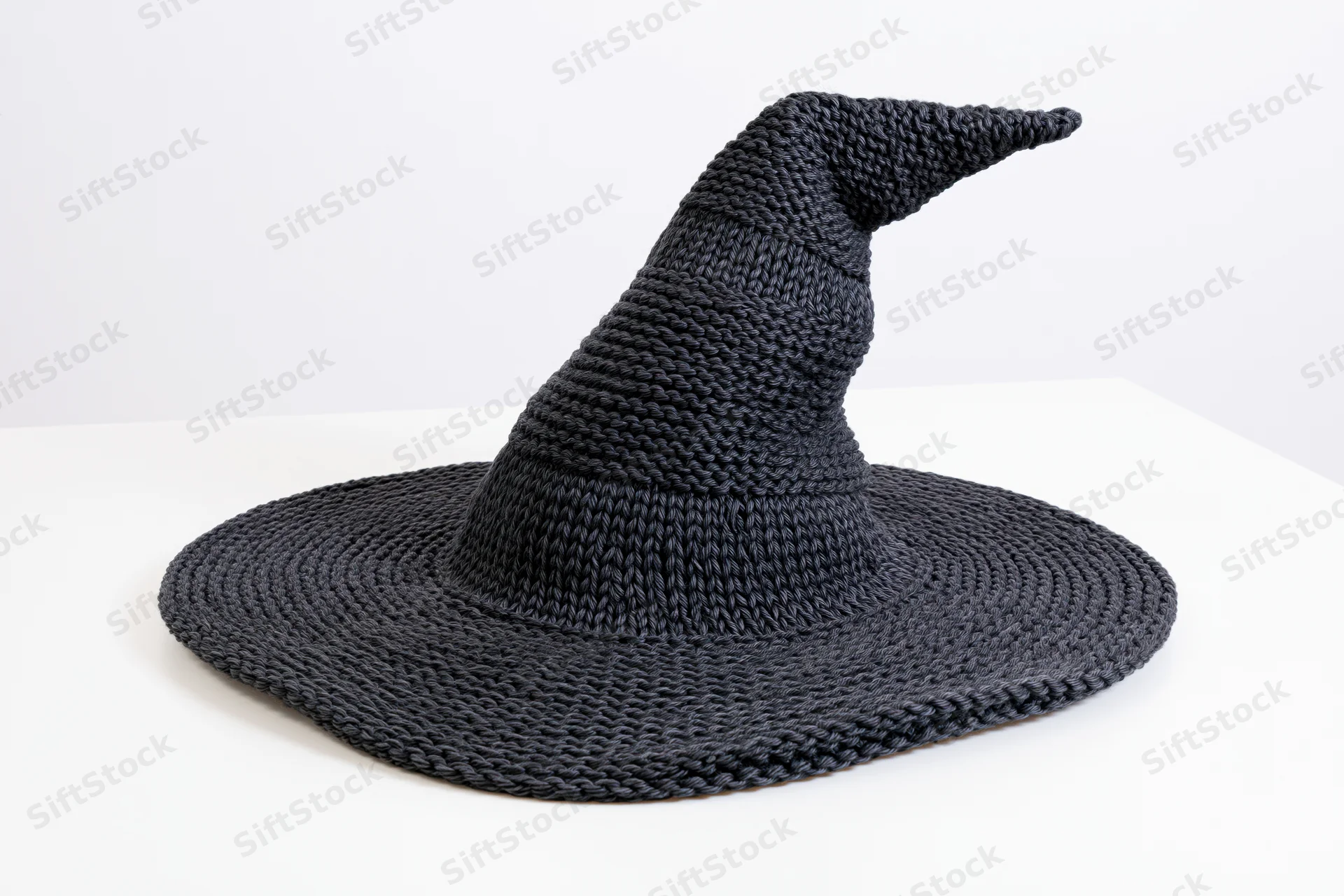 Dark charcoal knitted witch hat with wide brim and pointed tip on white surface