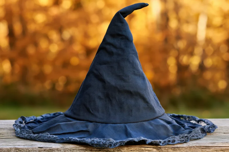 Dark navy fabric witch hat with pointed cone and lace trim resting on wooden bench outdoors in autumn light