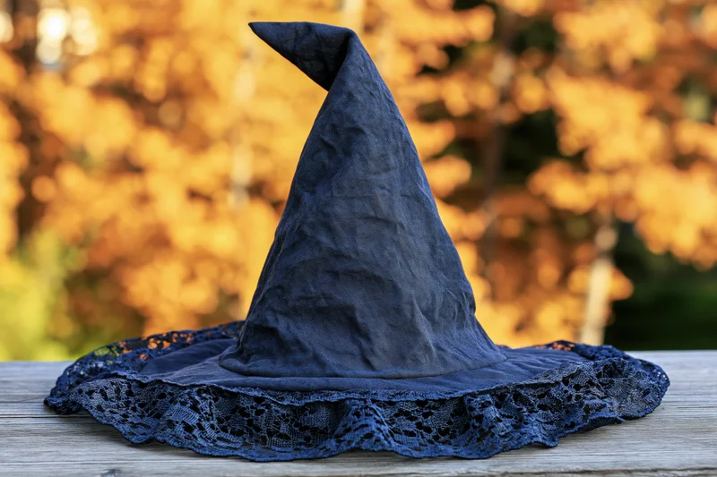 Dark navy fabric witch hat with pointed cone and lace trim resting on wooden table outdoors in autumn foliage