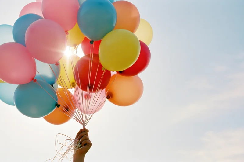 Hand holding a bunch of multicolored latex balloons against a bright sky
