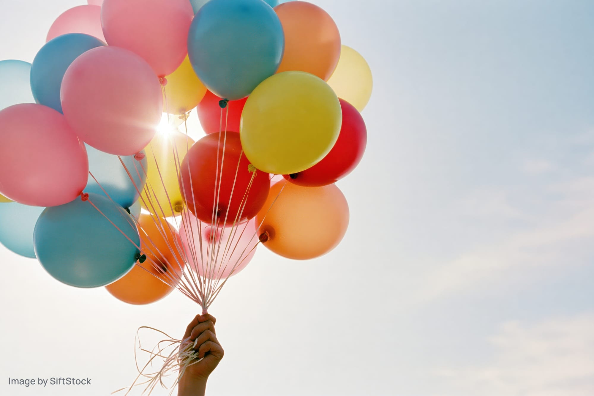 Hand holding a bunch of multicolored latex balloons against a bright sky