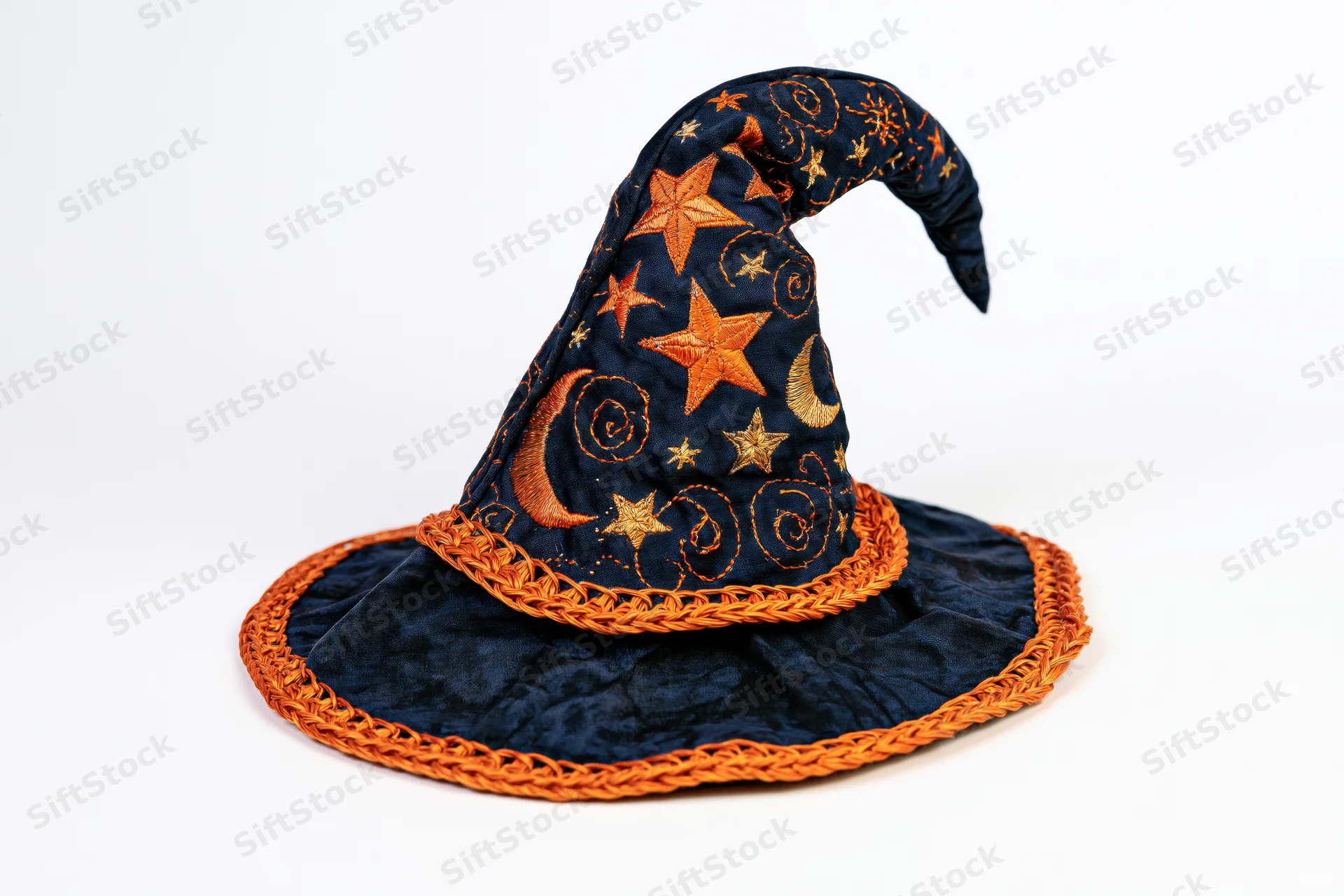 Handmade fabric witch hat with embroidered stars and moons, curved tip, orange braided trim, lying on white background