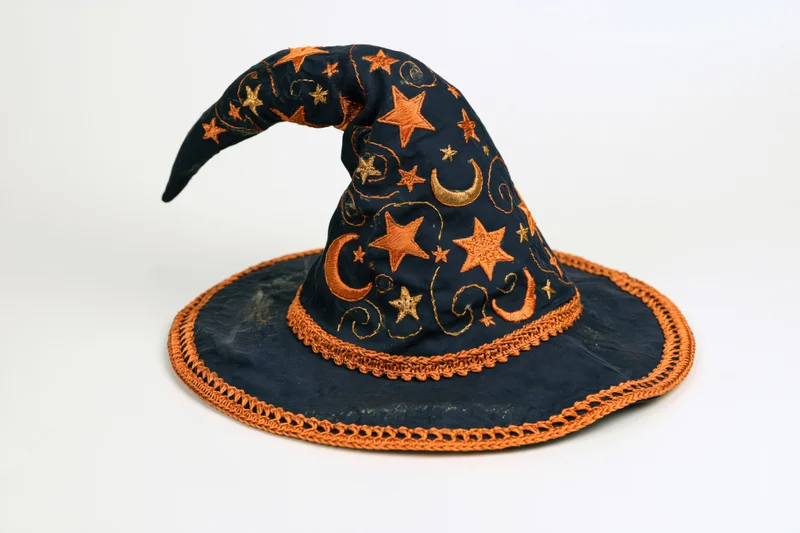 Handmade fabric witch hat with embroidered stars and moons, curved tip, navy and orange, isolated on white
