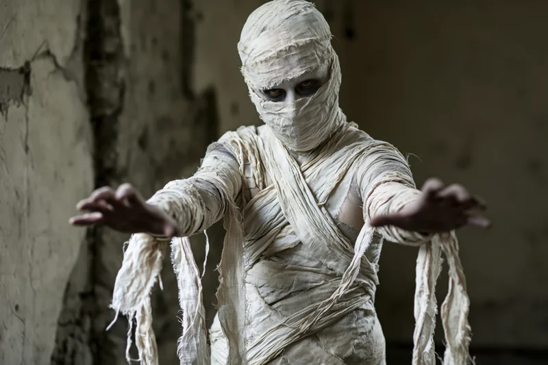 Man in mummy costume with arms outstretched in a crumbling stone room