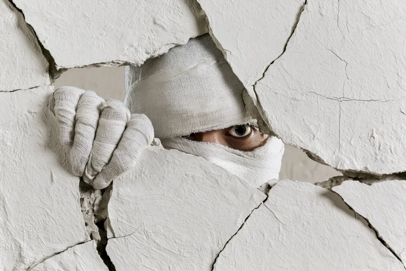 Mummy wrapped in bandages peering through cracked plaster wall