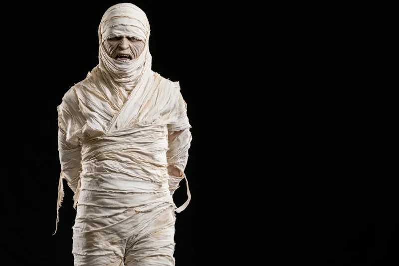 Mummy in full bandage costume standing upright against black background