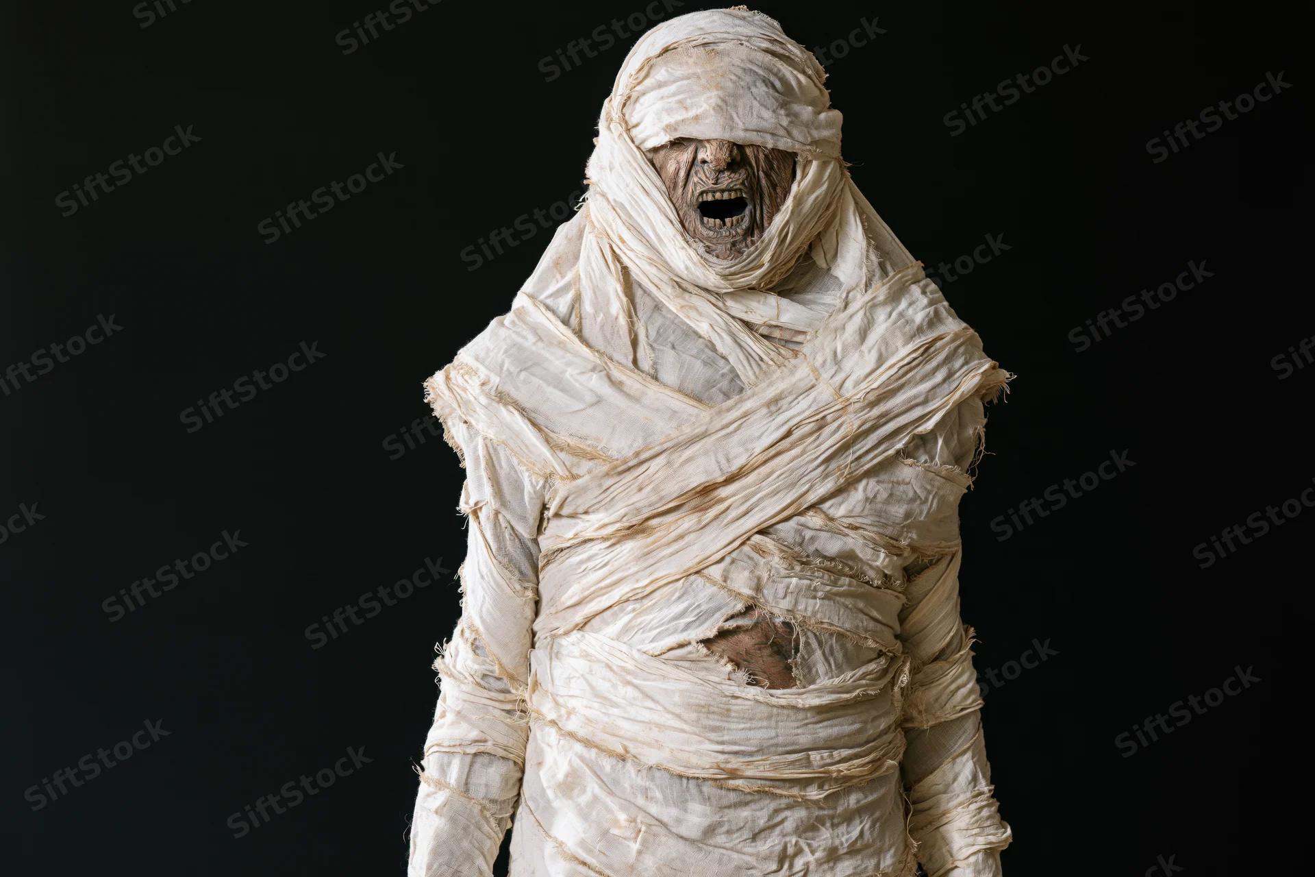 Mummy in full bandage costume screaming with mouth open against black background