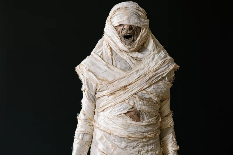 Mummy in full bandage costume screaming with mouth open against black background