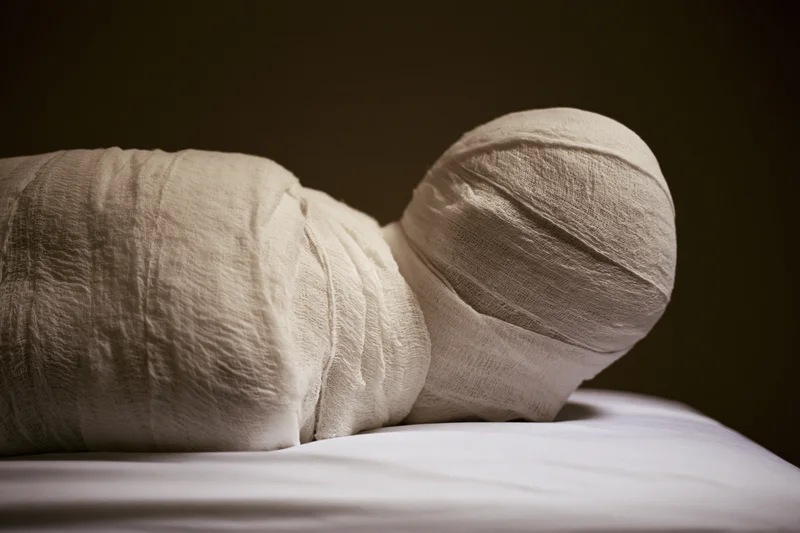 Mummy wrapped in linen bandages lying on a white surface in profile view