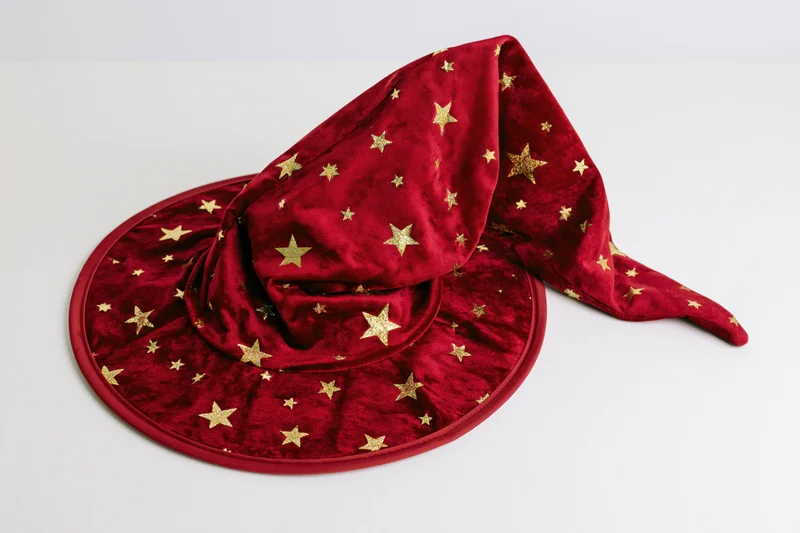 Red velvet witch hat with gold stars and curved drooping tip on white background