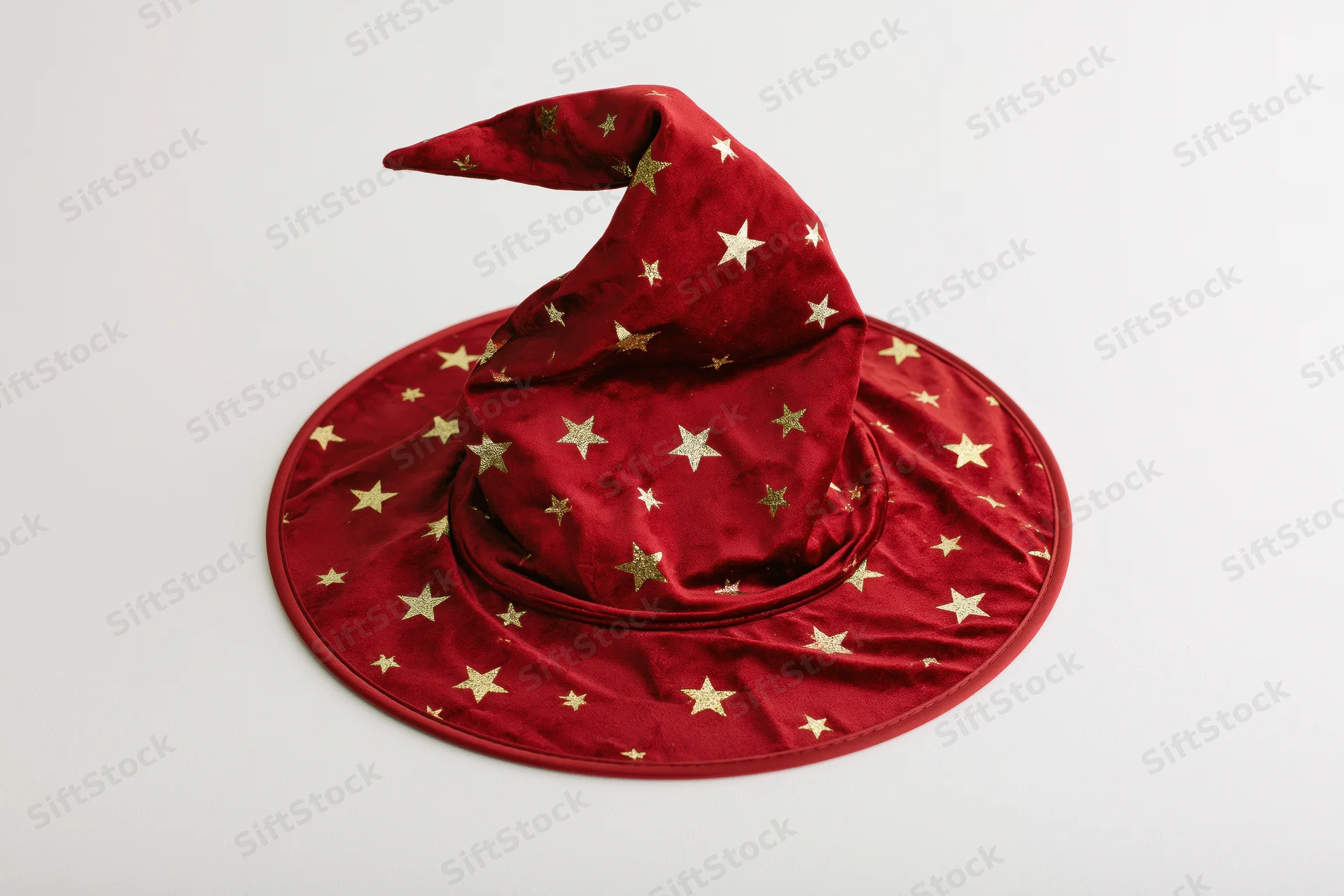 Red velvet witch hat with gold stars and curved drooping tip on white background