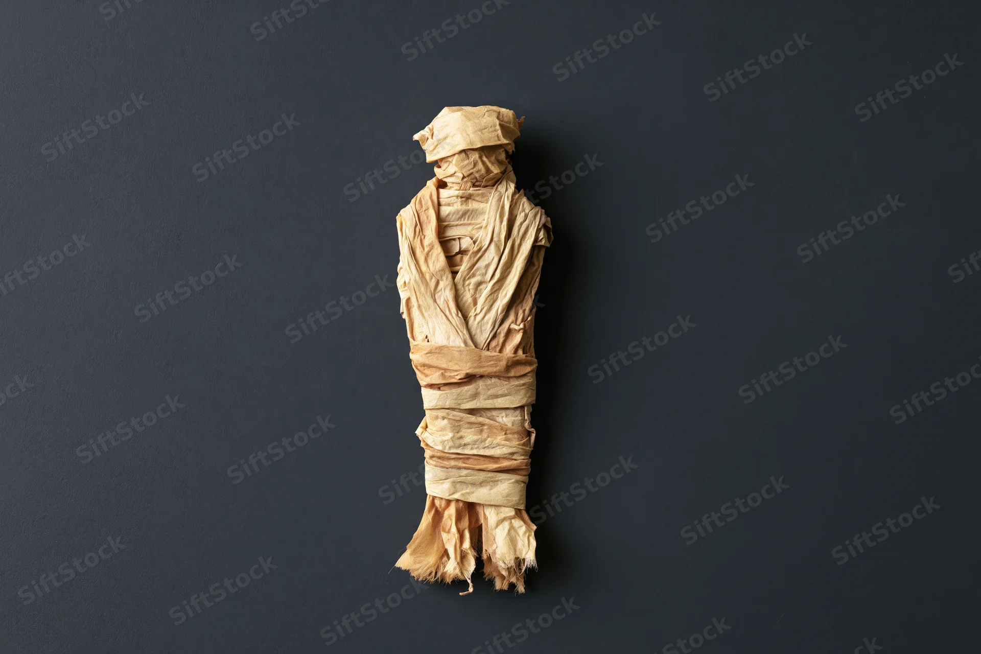 Handmade mummy figure wrapped in crumpled paper strips on dark background