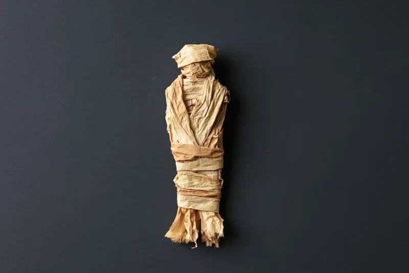 Handmade mummy figure wrapped in crumpled paper strips on dark background