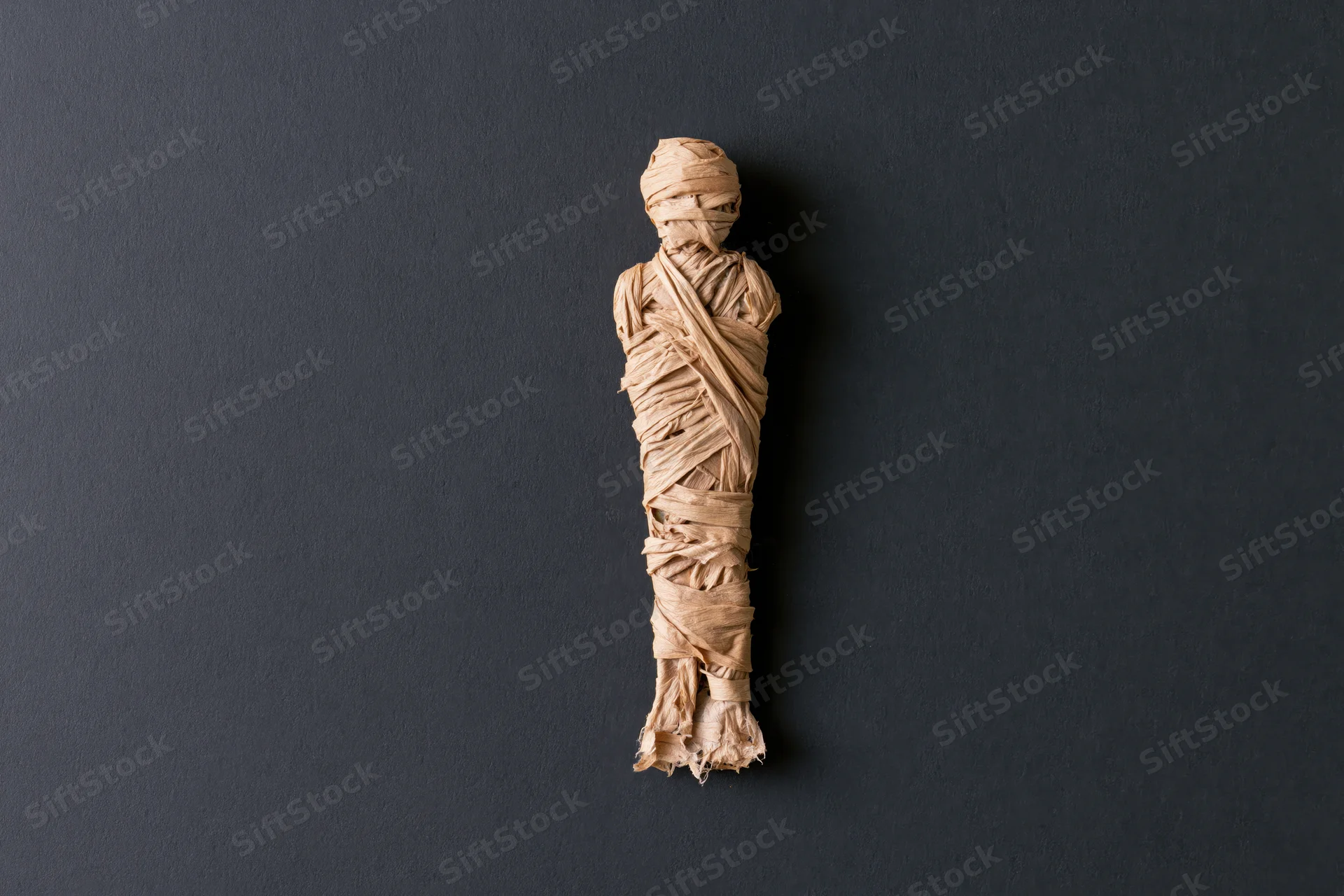 Small handmade mummy figure wrapped in linen strips on dark background