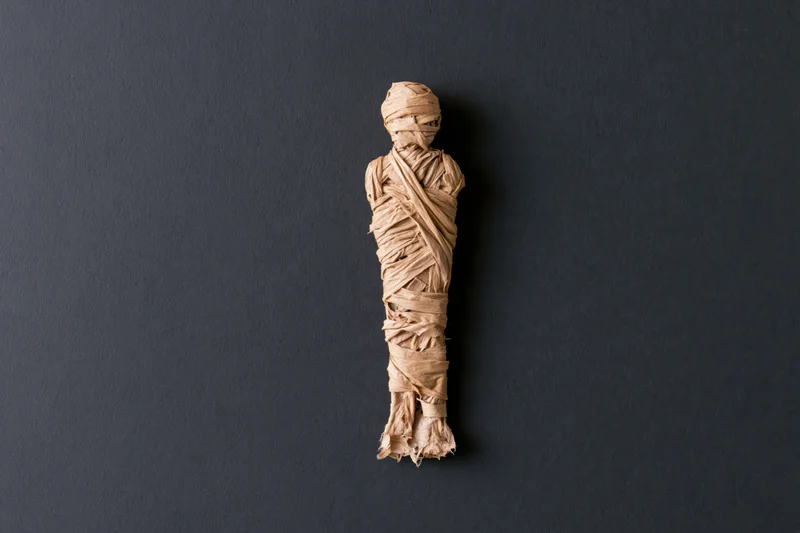 Small handmade mummy figure wrapped in linen strips on dark background