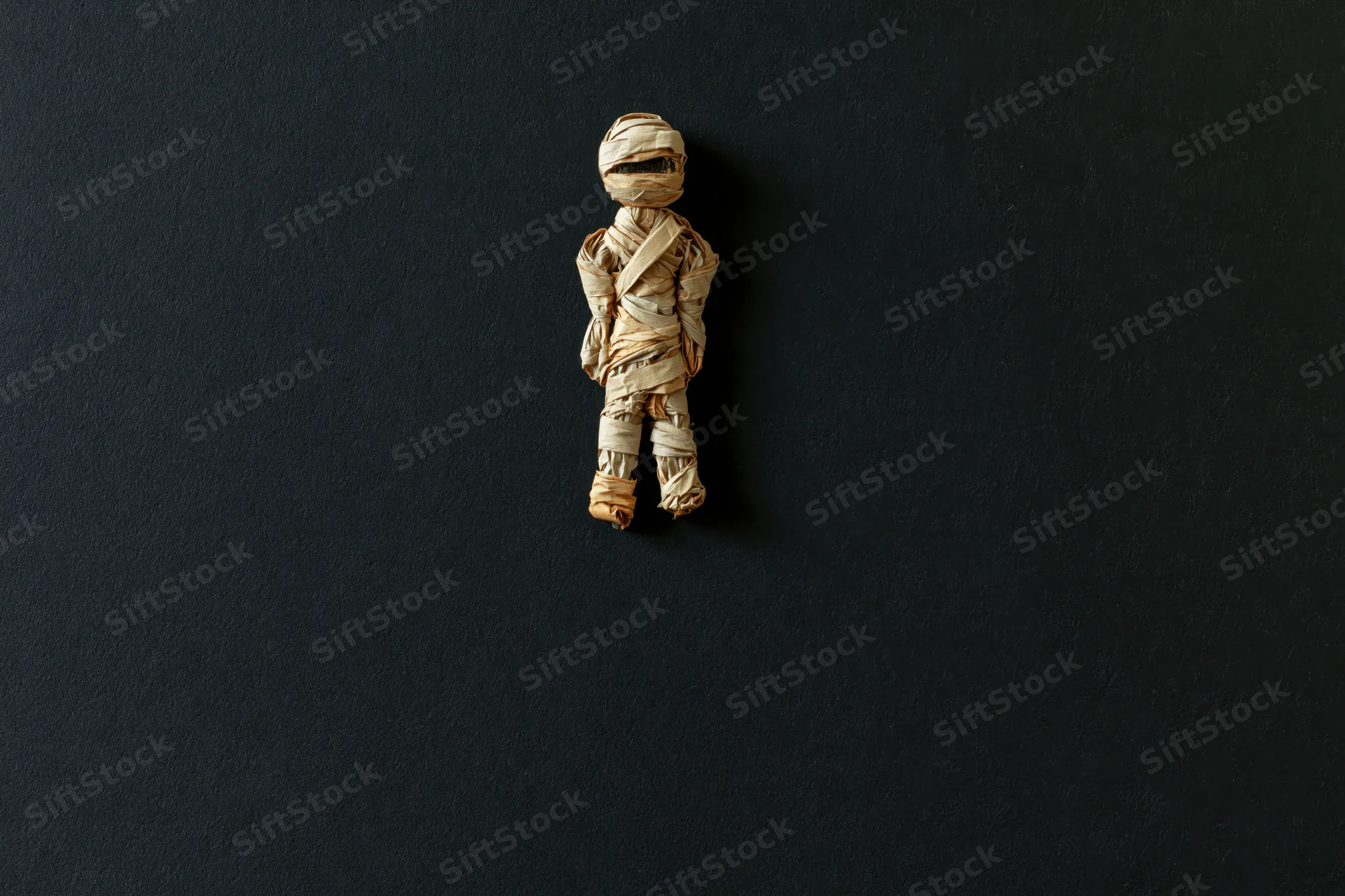 Small handmade mummy figurine wrapped in tan paper on dark background