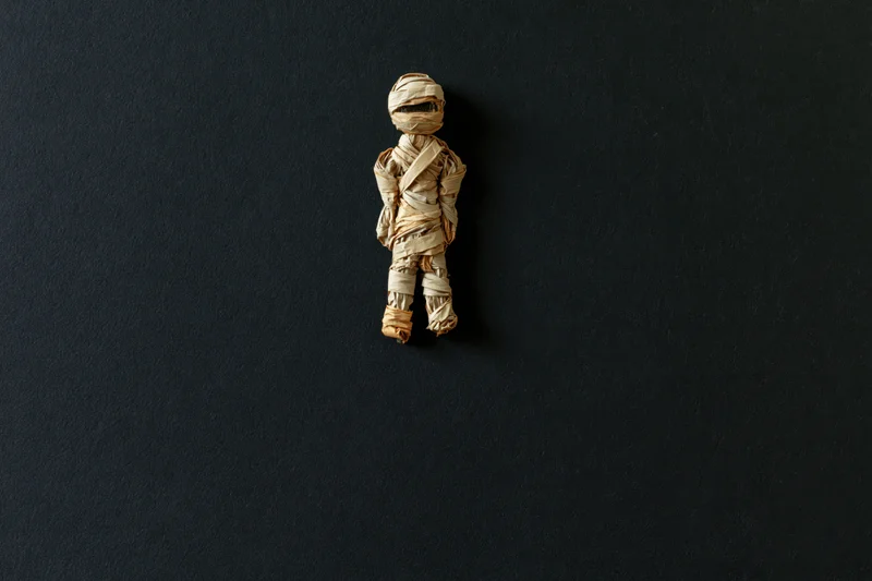 Small handmade mummy figurine wrapped in tan paper on dark background