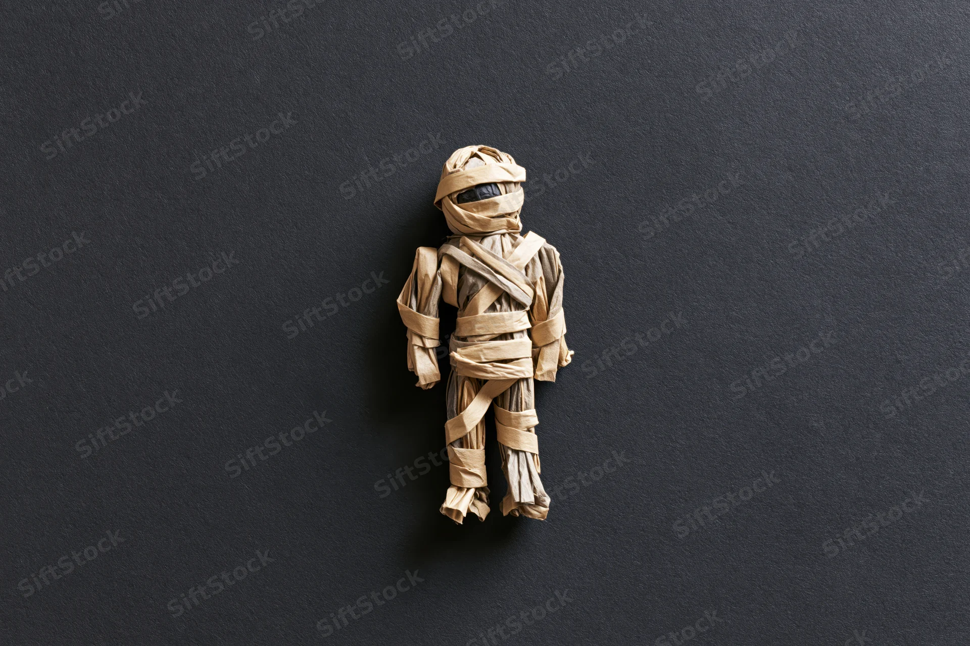 Handmade mummy figurine wrapped in tan paper on dark background