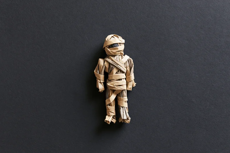 Handmade mummy figurine wrapped in tan paper on dark background