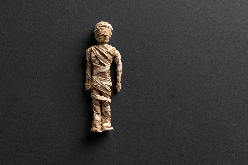 Handmade mummy figurine wrapped in tan paper against dark textured background