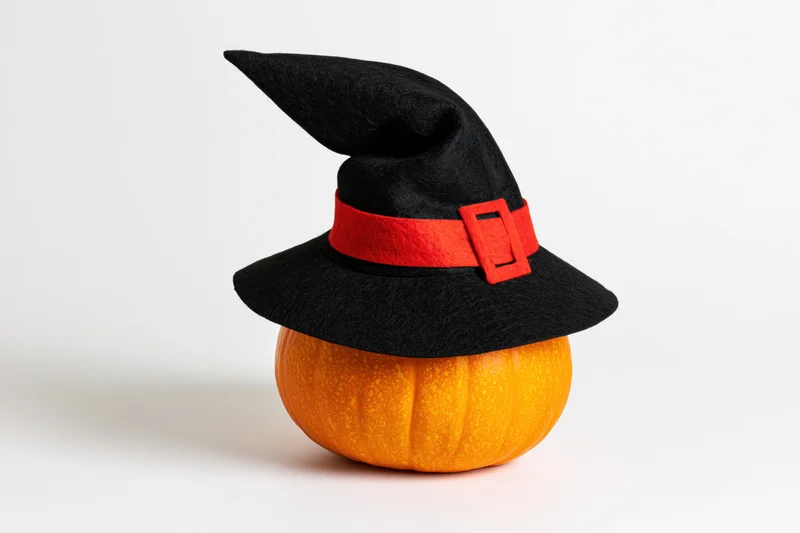 Small orange pumpkin wearing black witch hat on white background