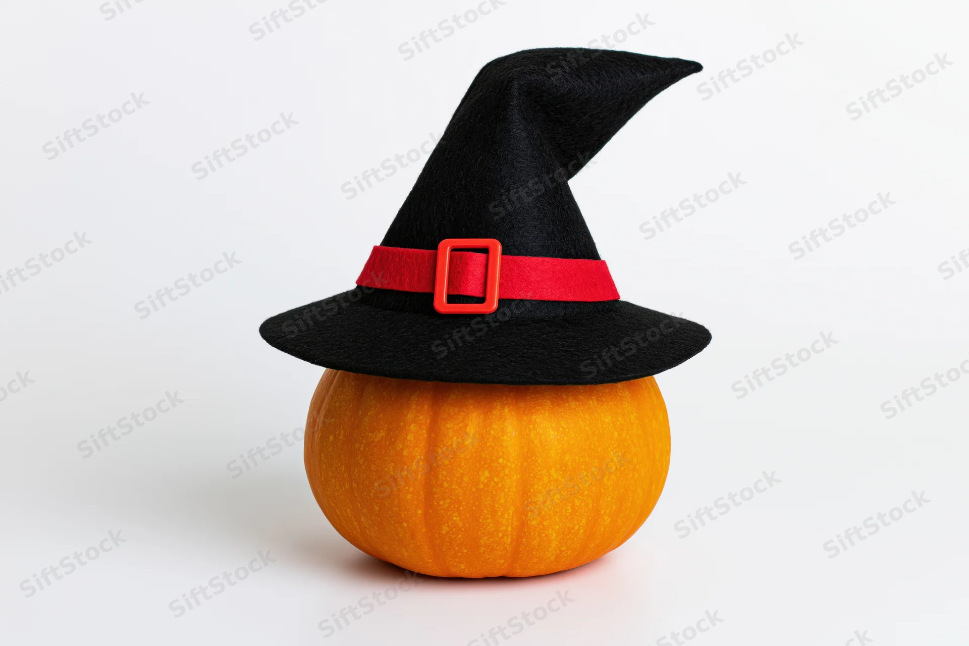 Small orange pumpkin wearing black witch hat with red buckle on white background