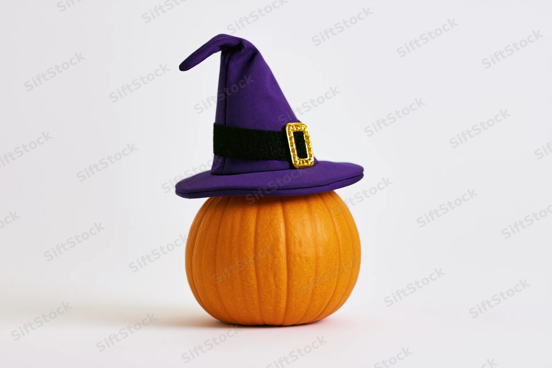 Small orange pumpkin wearing purple witch hat on white background