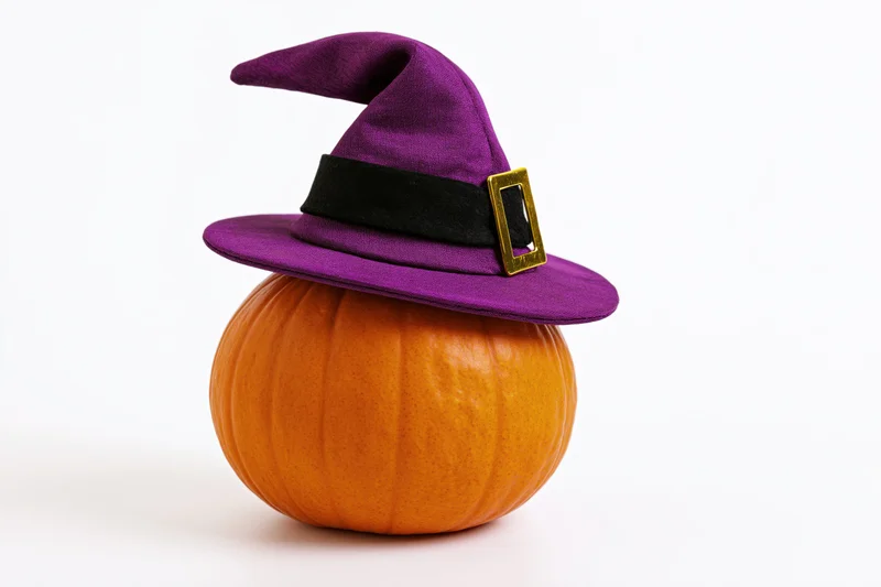 Small orange pumpkin wearing purple witch hat on white background