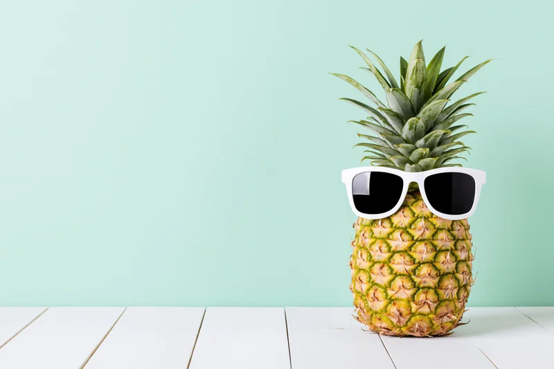 Pineapple wearing white sunglasses on a white wooden table against a mint green background