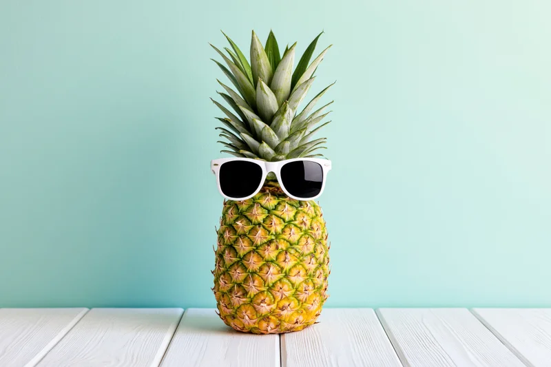 Pineapple wearing white-framed sunglasses on a white wooden table against a mint green background