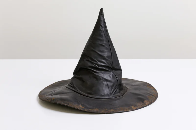Worn black pointed witch hat resting on white surface