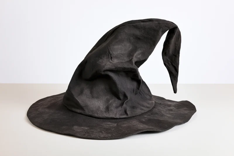 Worn black witch hat with bent drooping tip on white surface