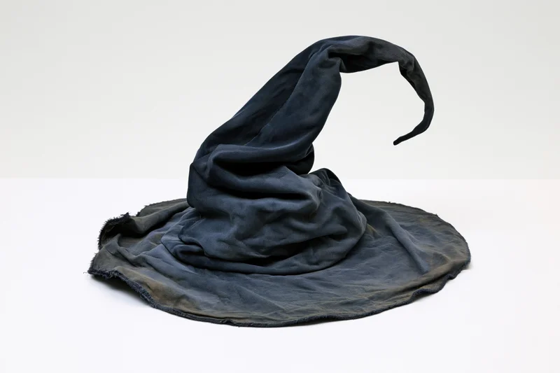 Worn black fabric wizard hat with tall curling pointed tip on white surface