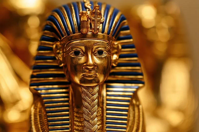 Golden funerary mask of an ancient egyptian pharaoh with blue striped headdress and cobra emblem