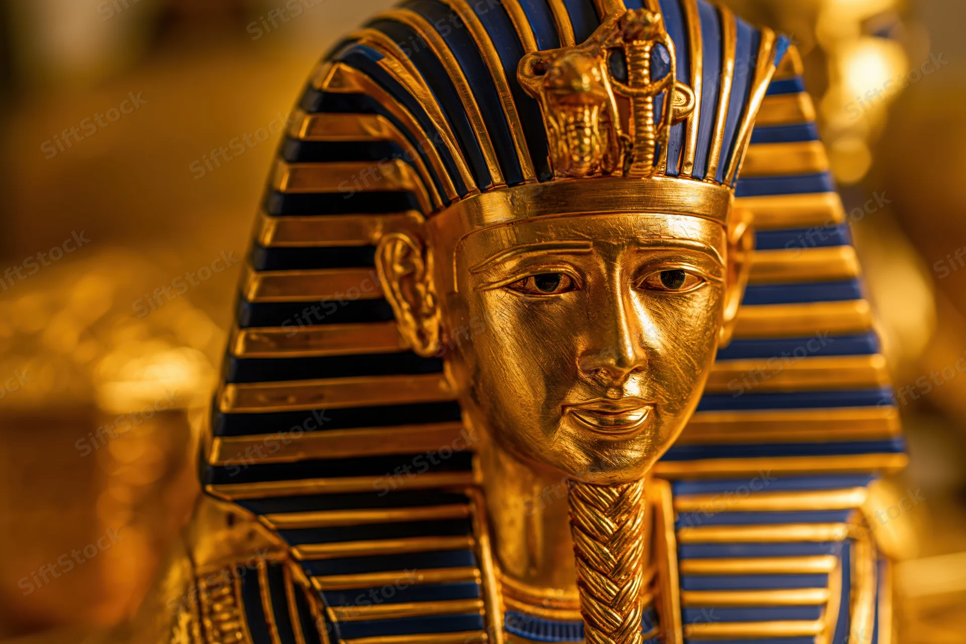 Golden pharaoh funerary mask with blue striped nemes headdress and cobra uraeus, displayed in museum setting