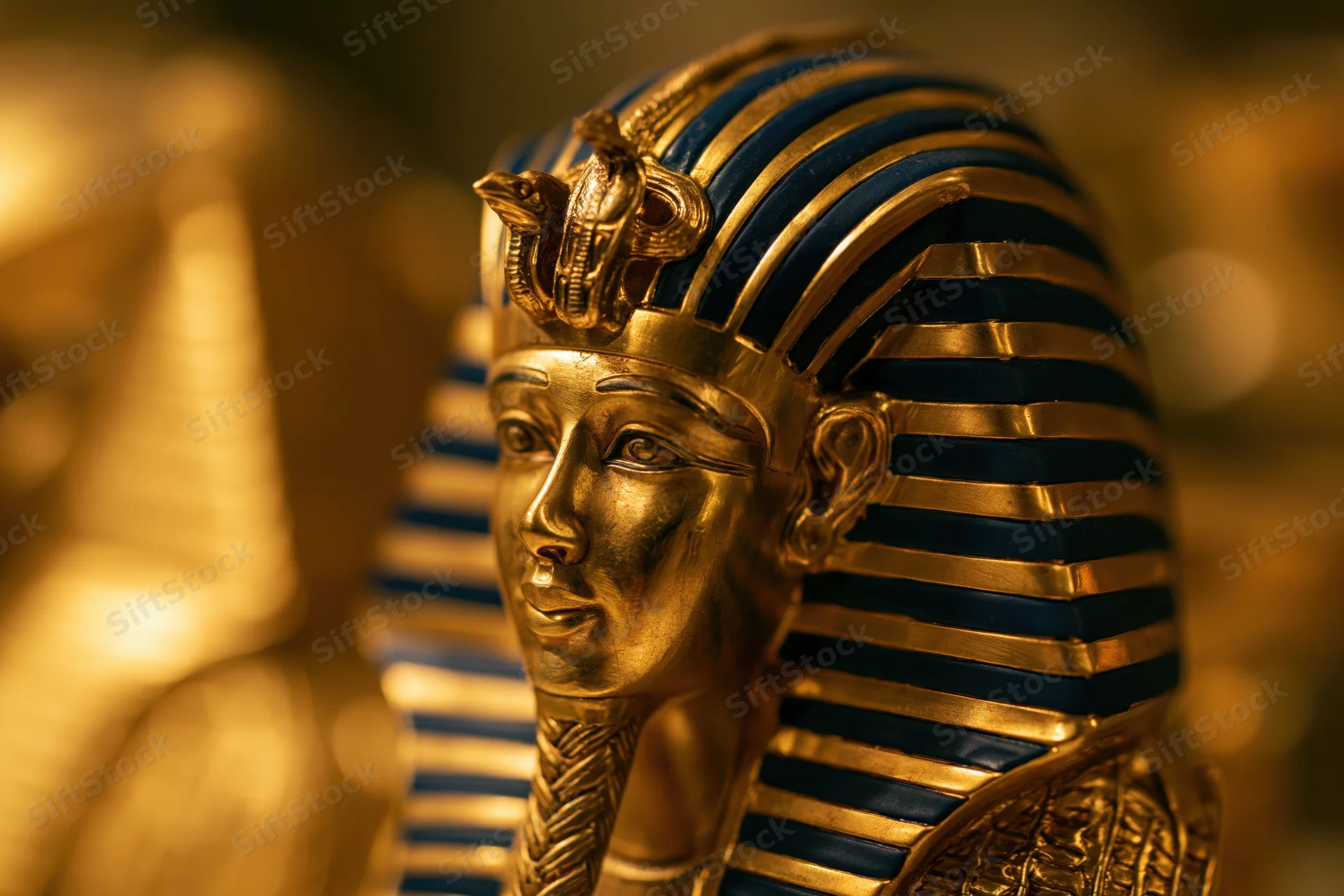 Golden pharaoh funerary mask with blue striped headdress and cobra emblem in museum display