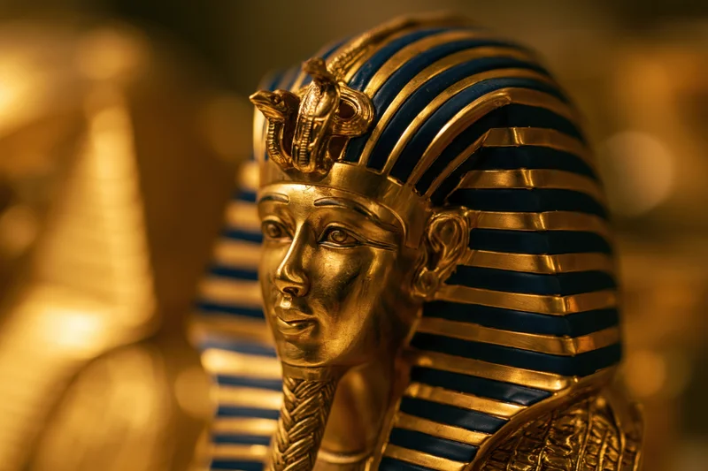 Golden pharaoh funerary mask with blue striped headdress and cobra emblem in museum display