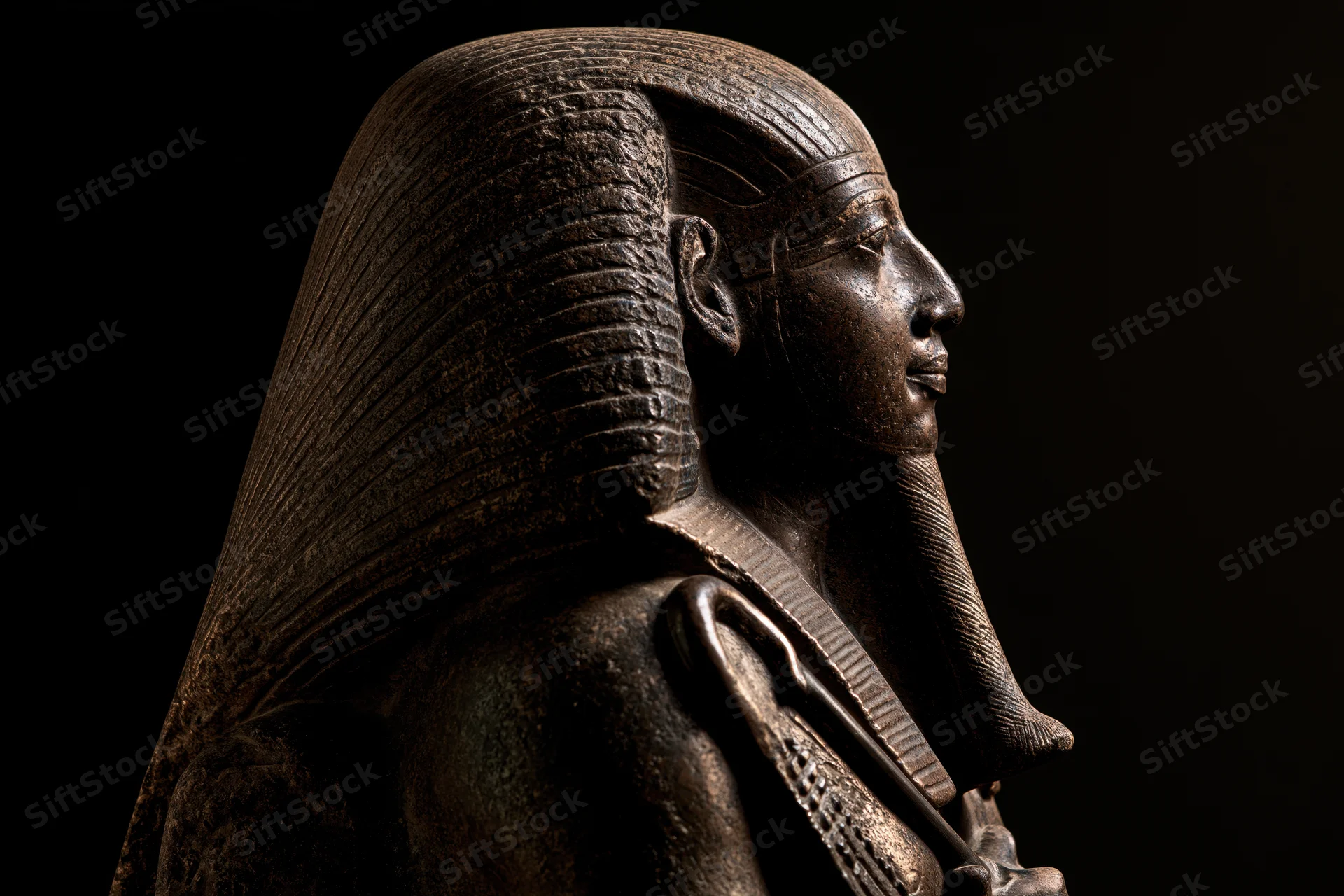 Ancient egyptian pharaoh statue in profile with nemes headdress and scepter against dark background