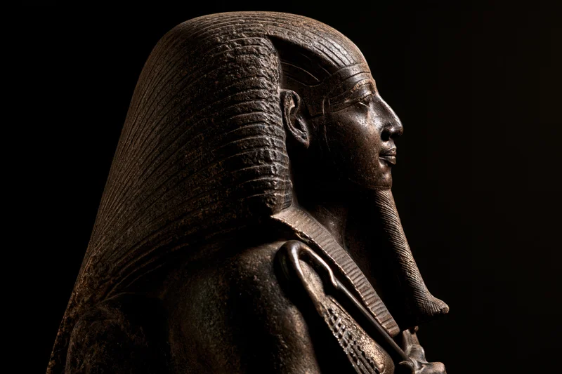 Ancient egyptian pharaoh statue in profile with nemes headdress and scepter against dark background