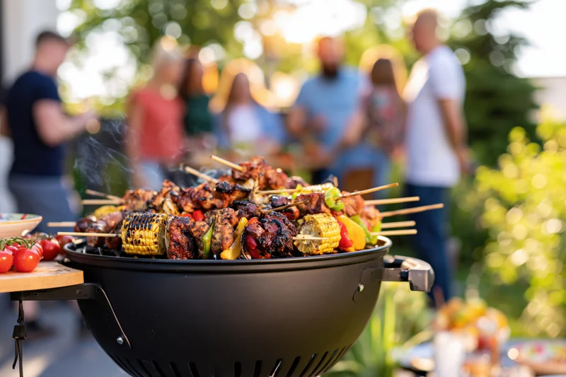 Charcoal grill filled with skewered meat and corn cooking outdoors at a backyard gathering