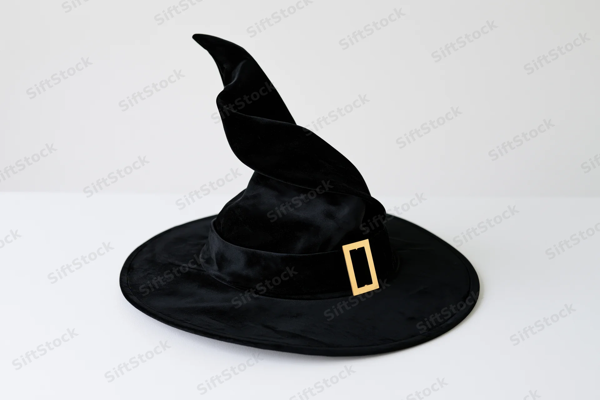 Black velvet witch hat with twisted pointed crown and wide brim on white surface