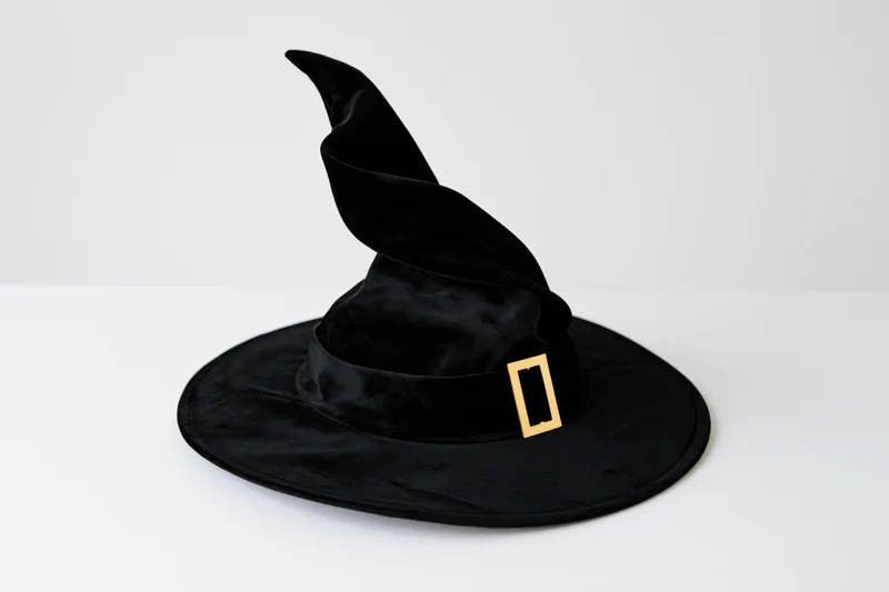 Black velvet witch hat with twisted pointed crown and wide brim on white surface