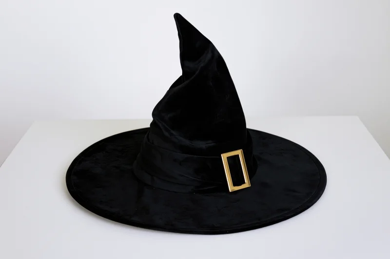 Black velvet witch hat with pointed crown and wide brim on white surface