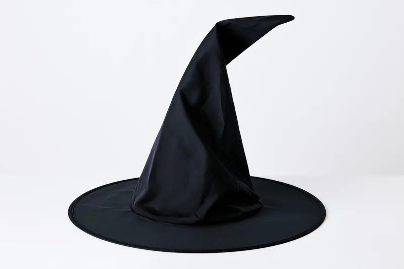 Black witch hat with tall pointed crown and wide flat brim on white surface
