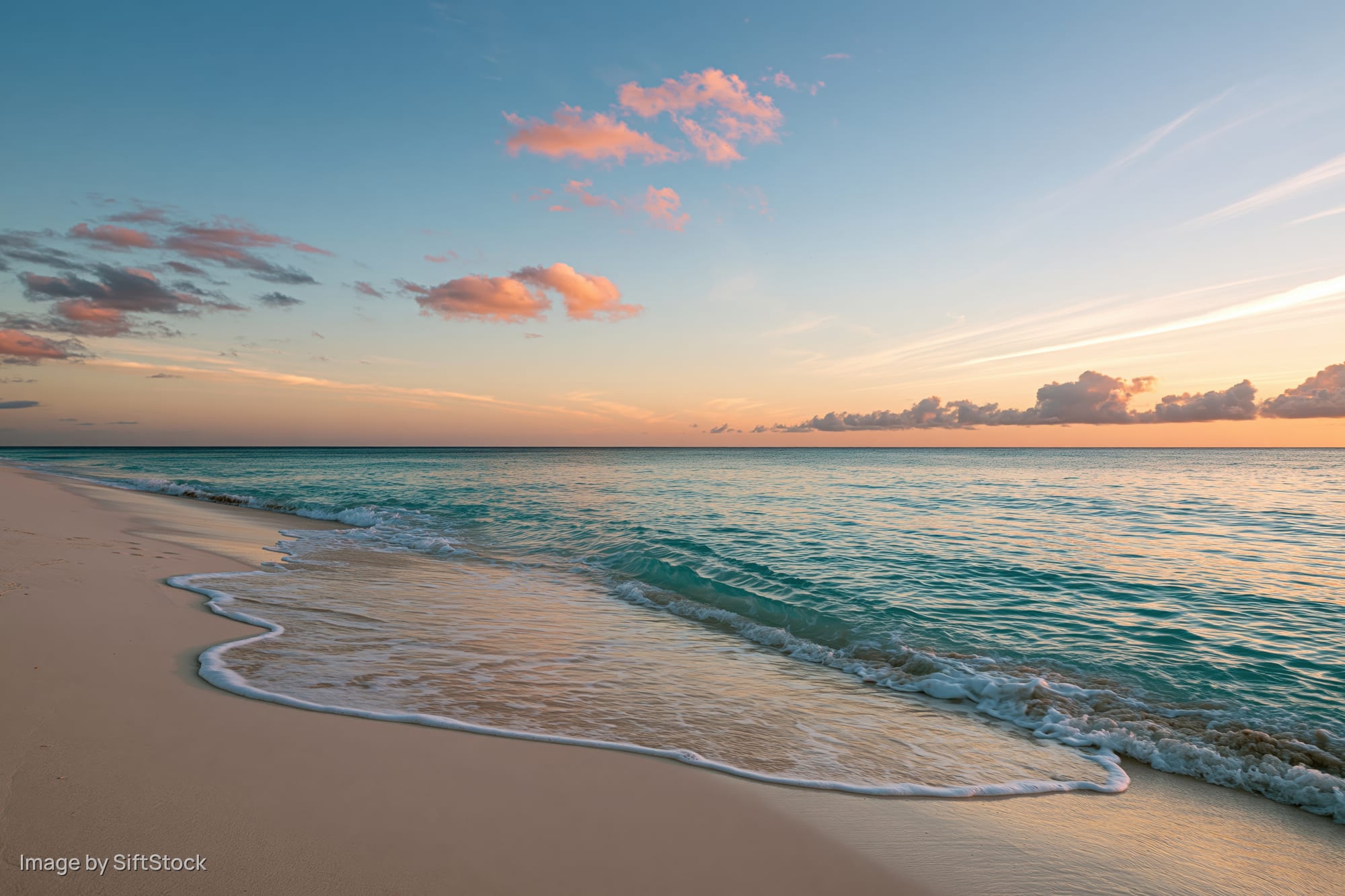 Gentle waves washing over sandy beach at sunset under pastel sky