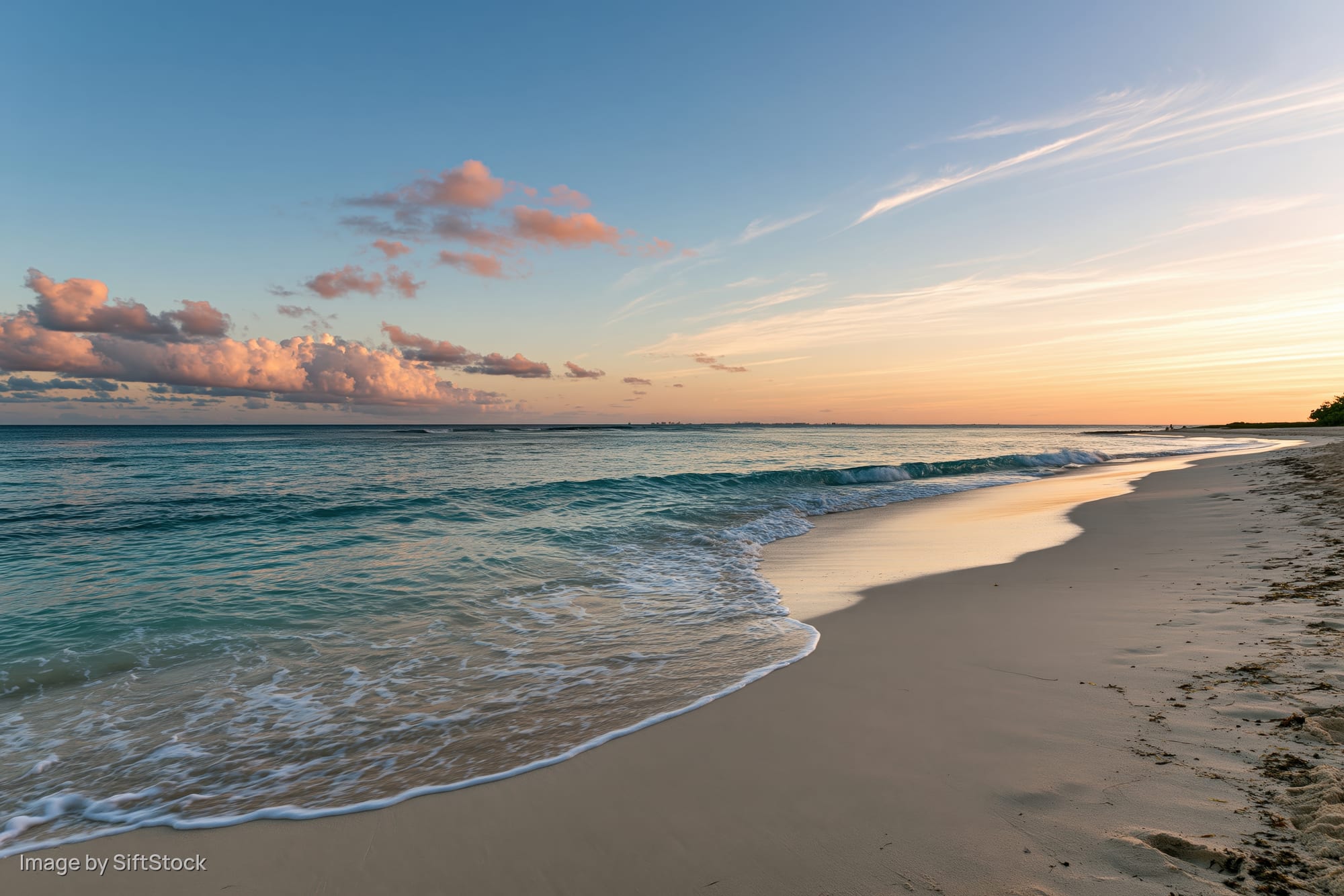 Gentle waves washing over sandy beach at sunset under pastel sky
