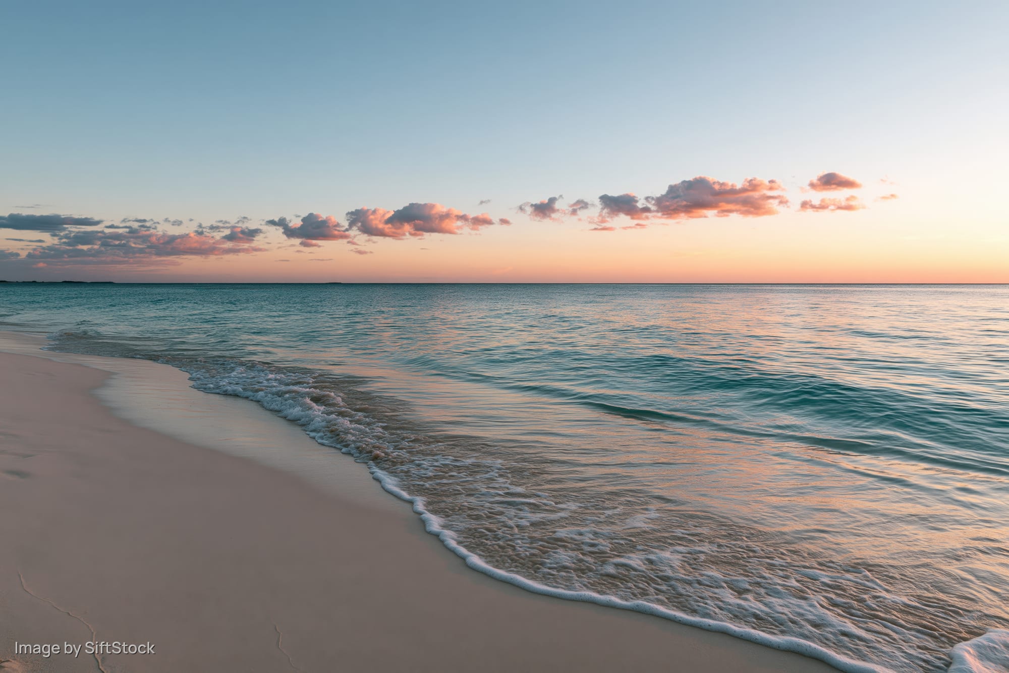 Gentle waves washing over sandy beach at sunset under pastel sky