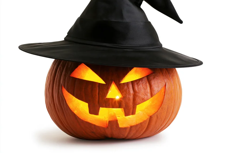 Carved pumpkin with glowing face wearing black witch hat on white background