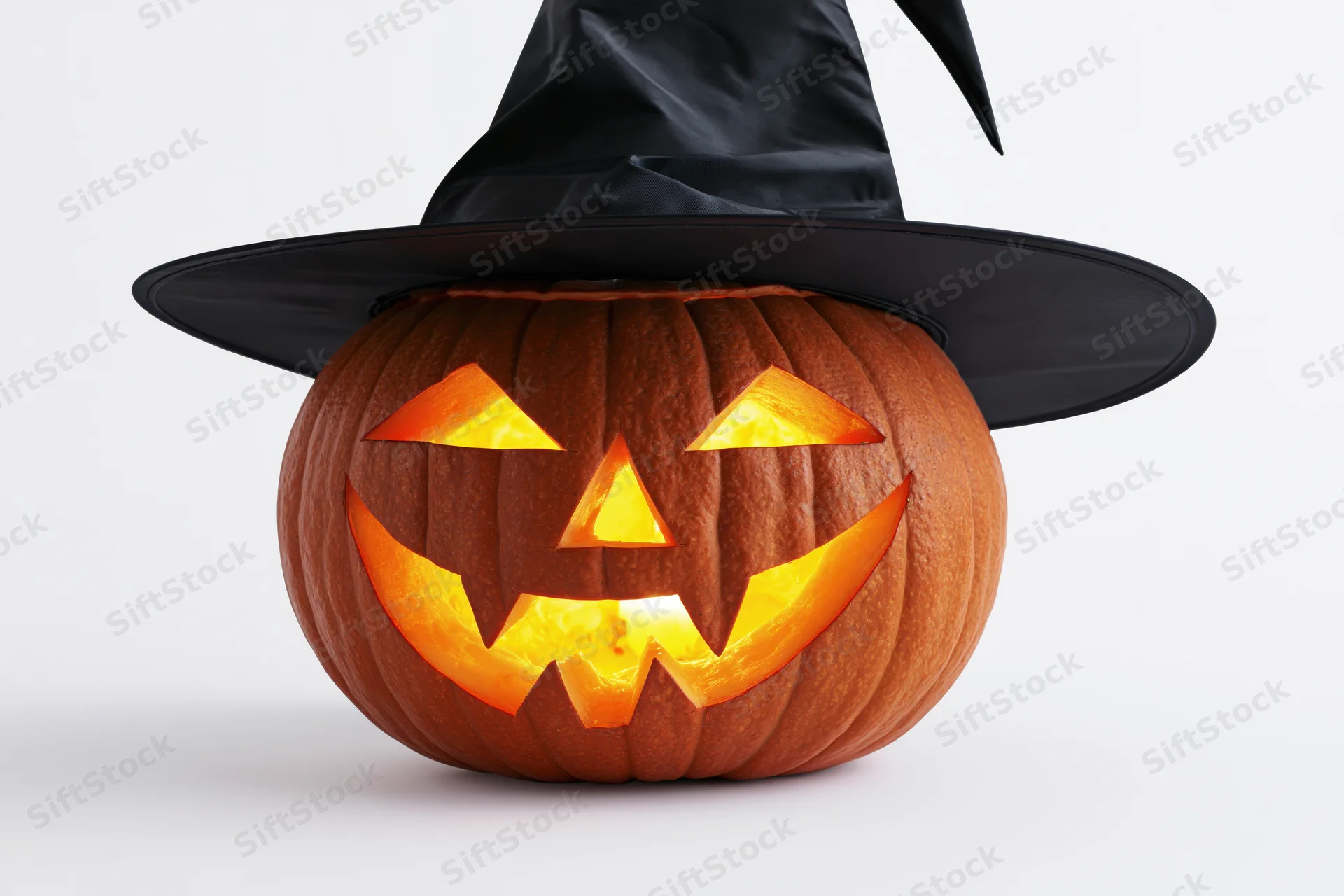 Carved pumpkin with glowing face wearing black witch hat on white background