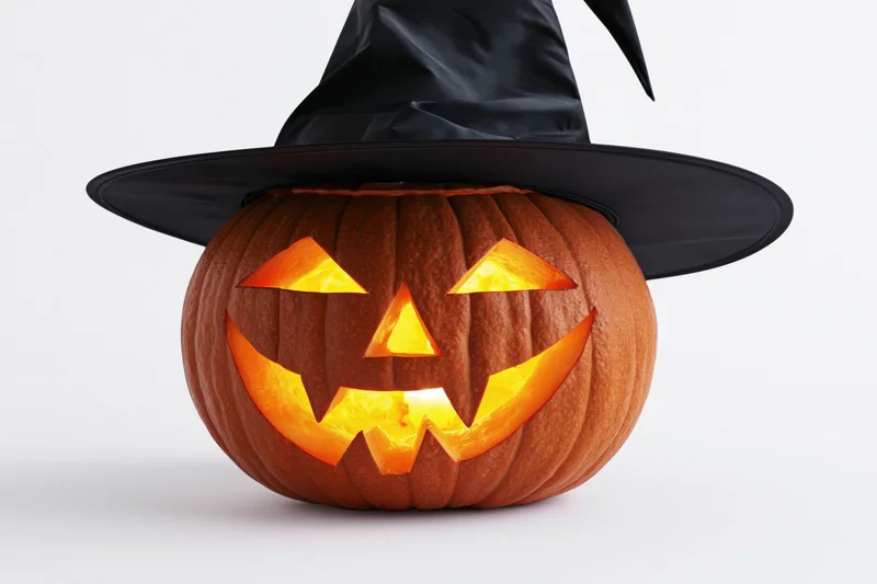 Carved pumpkin with glowing face wearing black witch hat on white background